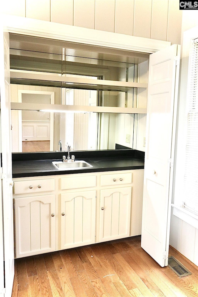 bar with white cabinets, sink, and light wood-type flooring