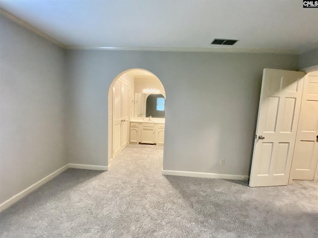 unfurnished bedroom featuring crown molding, ensuite bath, and light carpet