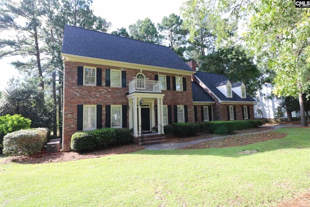 colonial inspired home with central air condition unit, a front lawn, and a balcony