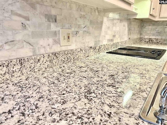 kitchen featuring white cabinetry, tile walls, light stone counters, and black stovetop