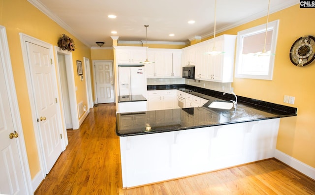 kitchen featuring white refrigerator with ice dispenser, kitchen peninsula, light hardwood / wood-style flooring, pendant lighting, and sink