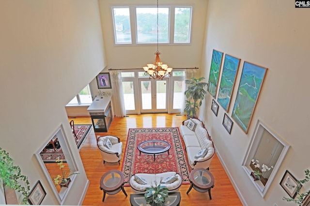 living room with a notable chandelier, light wood-type flooring, and a towering ceiling