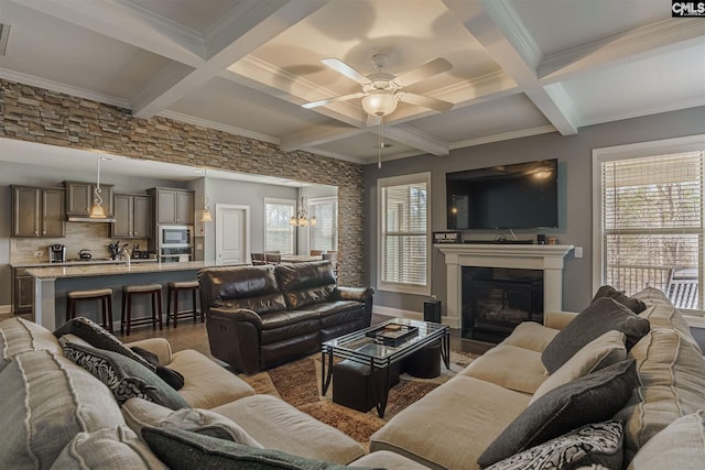 living room with coffered ceiling, ceiling fan with notable chandelier, ornamental molding, and beamed ceiling