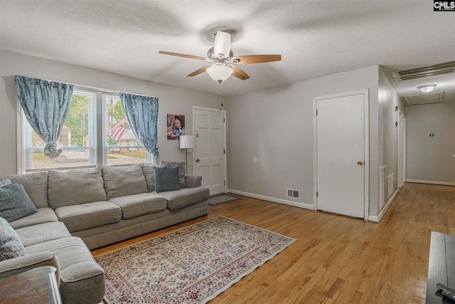 living room with a textured ceiling, ceiling fan, and light wood-type flooring