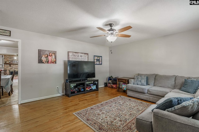 living room featuring a textured ceiling, a brick fireplace, ceiling fan, and light wood-type flooring