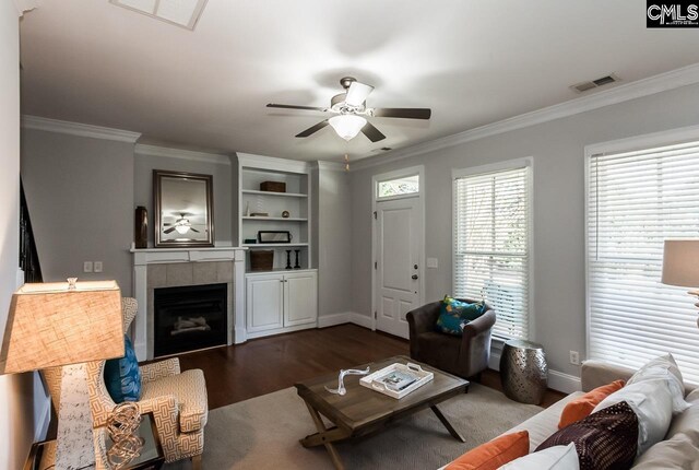 living room featuring ceiling fan, ornamental molding, a tiled fireplace, and dark hardwood / wood-style flooring