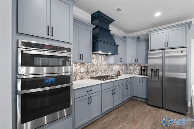 kitchen with gray cabinetry, backsplash, crown molding, dark hardwood / wood-style floors, and stainless steel appliances