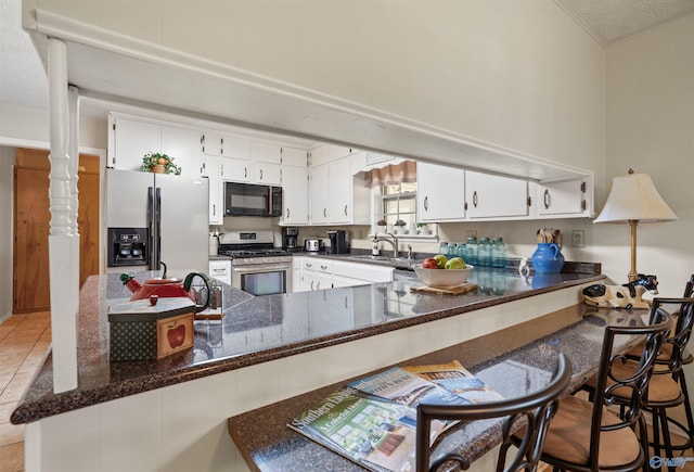 kitchen with black microwave, stainless steel gas range, a peninsula, white cabinetry, and refrigerator with ice dispenser