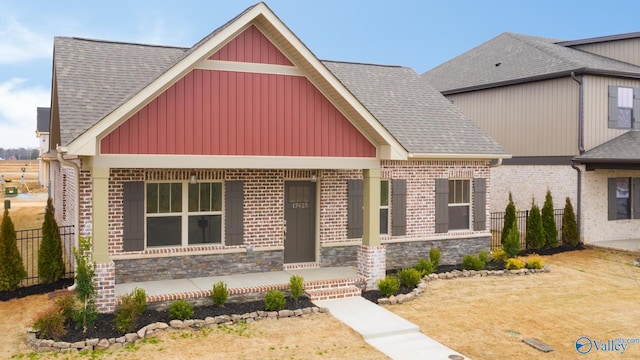 view of front facade with fence, covered porch, stone siding, and a shingled roof