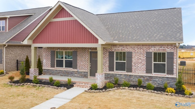 craftsman inspired home featuring fence, a porch, a shingled roof, stone siding, and board and batten siding