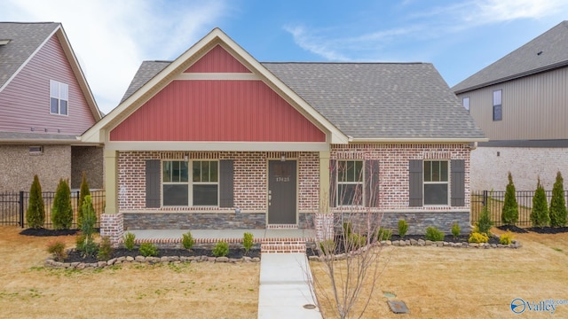 craftsman house with stone siding, covered porch, a shingled roof, and fence