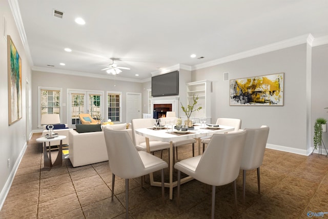 dining area with a warm lit fireplace, baseboards, visible vents, and ornamental molding