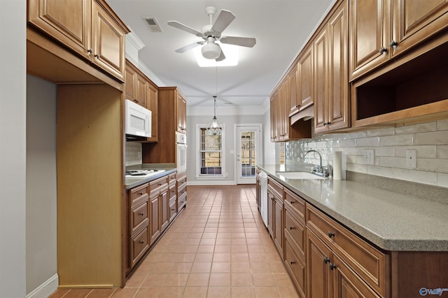 kitchen featuring brown cabinets, light tile patterned floors, backsplash, a sink, and white appliances