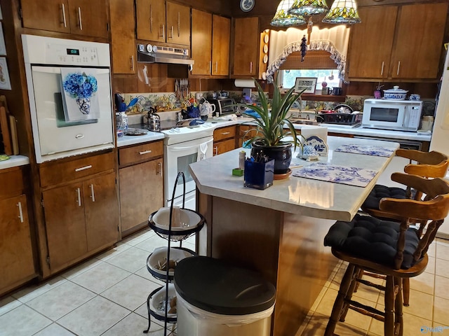 kitchen with white appliances, a breakfast bar area, and light tile patterned flooring