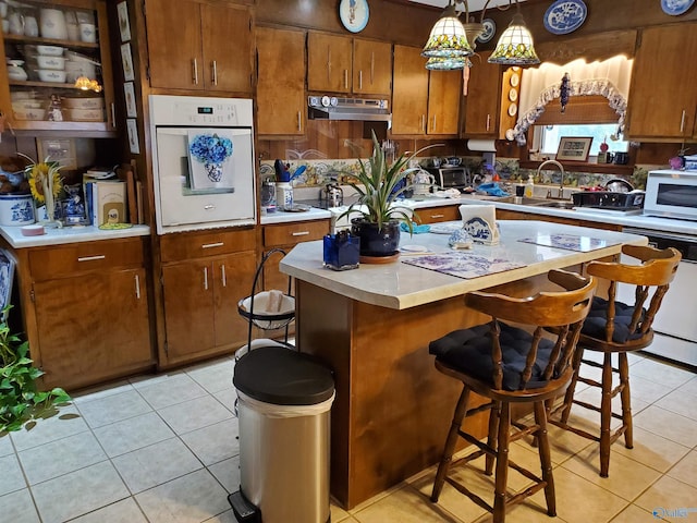 kitchen with a breakfast bar area, hanging light fixtures, a center island, light tile patterned floors, and white appliances