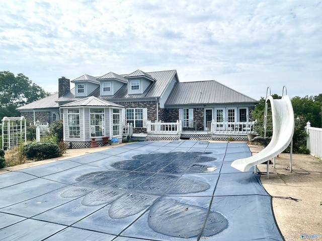 rear view of house with metal roof, fence, a deck, and a standing seam roof