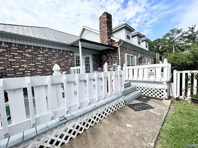 view of property exterior featuring a chimney, a deck, and brick siding