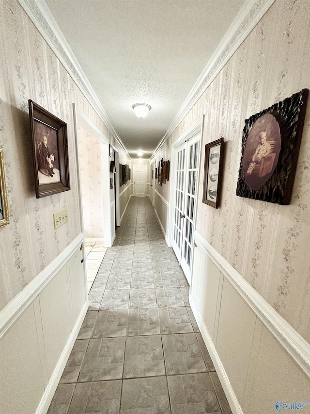 corridor with wainscoting, a textured ceiling, and wallpapered walls