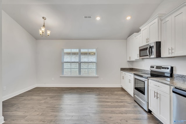 kitchen featuring stainless steel appliances, vaulted ceiling, wood-type flooring, dark stone countertops, and white cabinetry