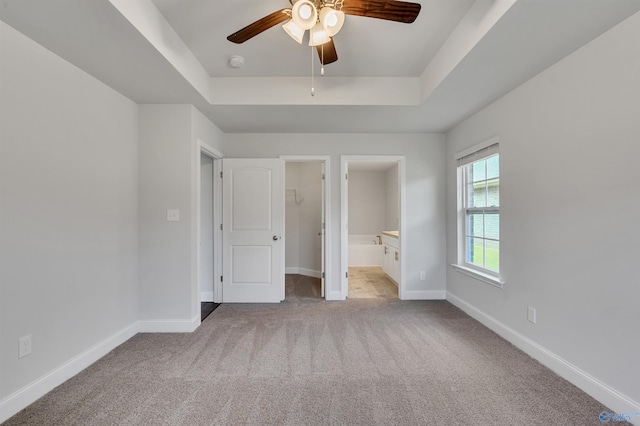 unfurnished bedroom with ensuite bath, ceiling fan, a raised ceiling, a walk in closet, and light carpet