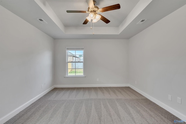 carpeted spare room with a raised ceiling and ceiling fan