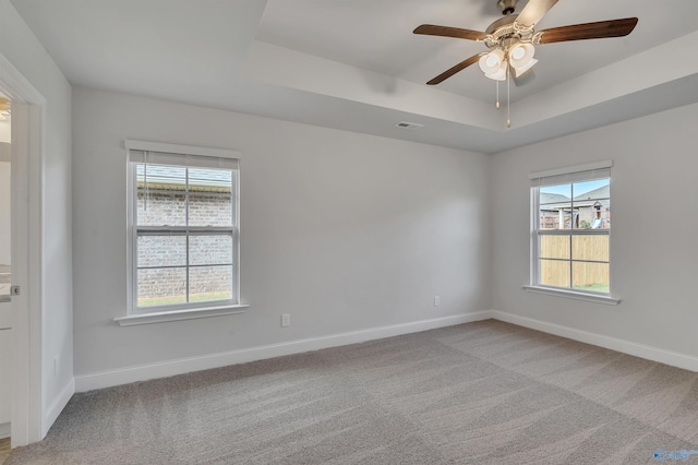 empty room with a tray ceiling, light carpet, and ceiling fan