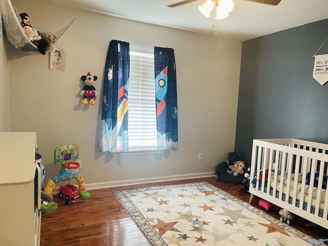 bedroom with ceiling fan, wood-type flooring, a crib, and a textured ceiling