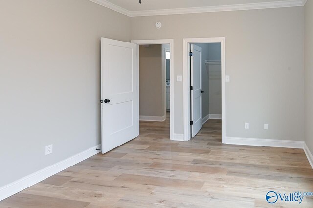 unfurnished bedroom featuring a walk in closet, light hardwood / wood-style flooring, ornamental molding, and a closet