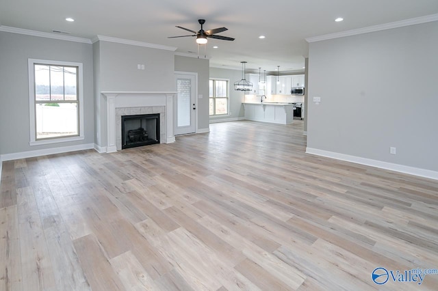 unfurnished living room featuring light hardwood / wood-style floors, ornamental molding, a tile fireplace, and ceiling fan