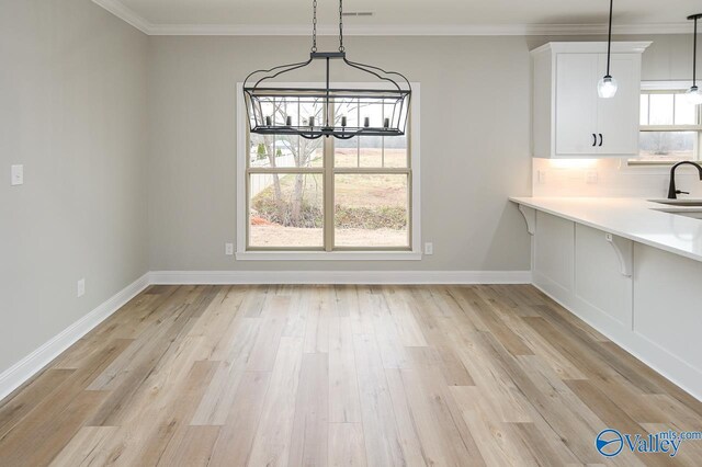 unfurnished dining area featuring light hardwood / wood-style floors, sink, an inviting chandelier, and crown molding