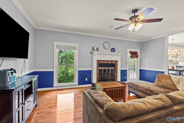 living room with a brick fireplace, a textured ceiling, light wood-type flooring, and ornamental molding