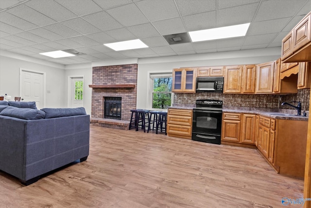 kitchen with sink, light hardwood / wood-style flooring, backsplash, black appliances, and a fireplace