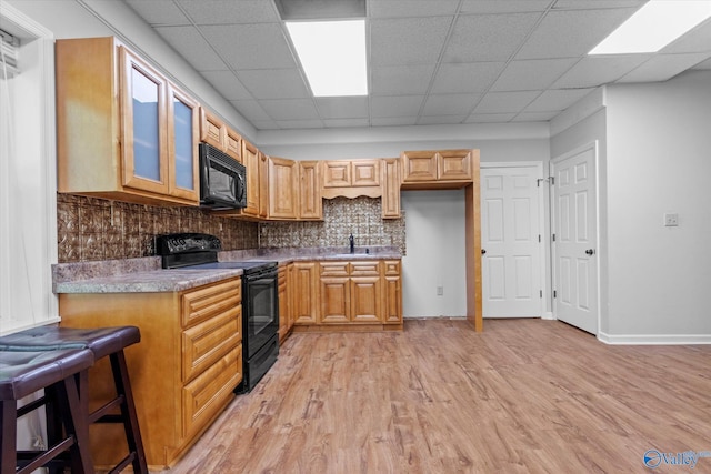 kitchen featuring sink, light hardwood / wood-style flooring, black appliances, a drop ceiling, and a breakfast bar area