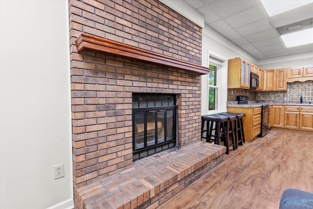 unfurnished living room with a paneled ceiling, sink, light hardwood / wood-style flooring, and a brick fireplace