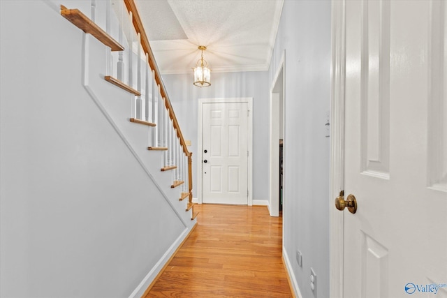 interior space with an inviting chandelier, light wood-type flooring, a textured ceiling, and crown molding