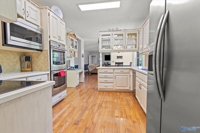 kitchen featuring white cabinets, kitchen peninsula, light hardwood / wood-style flooring, stainless steel appliances, and backsplash