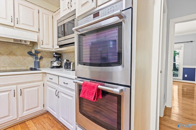 kitchen featuring light hardwood / wood-style floors, tasteful backsplash, white cabinetry, appliances with stainless steel finishes, and crown molding