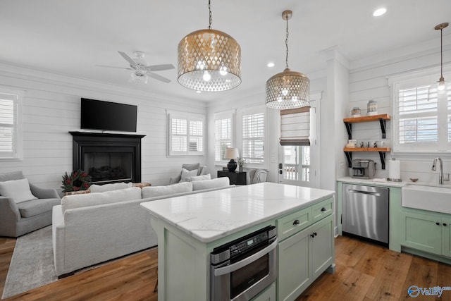 kitchen featuring hardwood / wood-style flooring, a sink, green cabinets, open floor plan, and appliances with stainless steel finishes