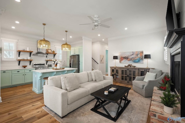 living room featuring light wood-style flooring, ceiling fan, stairs, crown molding, and recessed lighting