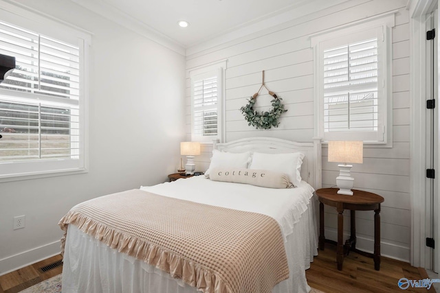 bedroom with ornamental molding, visible vents, baseboards, and wood finished floors