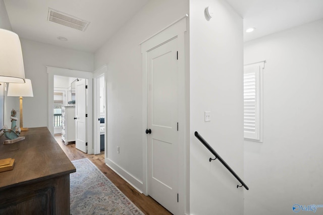 hallway with baseboards, visible vents, wood finished floors, an upstairs landing, and recessed lighting