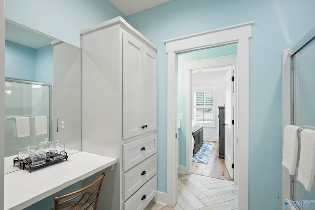 full bathroom with wood finished floors, a shower with shower door, and baseboards