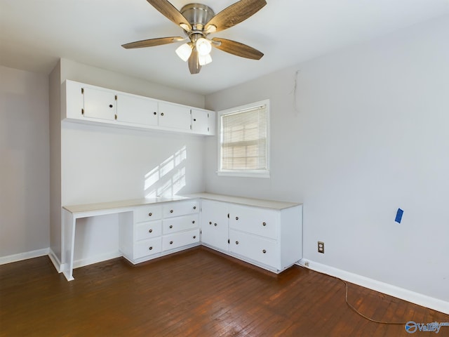 unfurnished office featuring dark wood-type flooring, ceiling fan, and built in desk