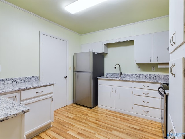 kitchen with appliances with stainless steel finishes, sink, white cabinets, crown molding, and light hardwood / wood-style flooring