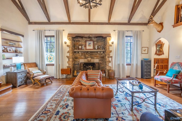 living room featuring a stone fireplace, plenty of natural light, wood-type flooring, and beam ceiling