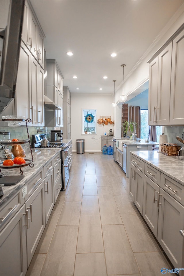 kitchen featuring stainless steel range with gas stovetop, light stone counters, tasteful backsplash, decorative light fixtures, and gray cabinets