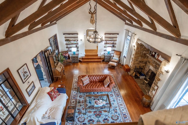 living room with hardwood / wood-style floors, a stone fireplace, an inviting chandelier, and high vaulted ceiling