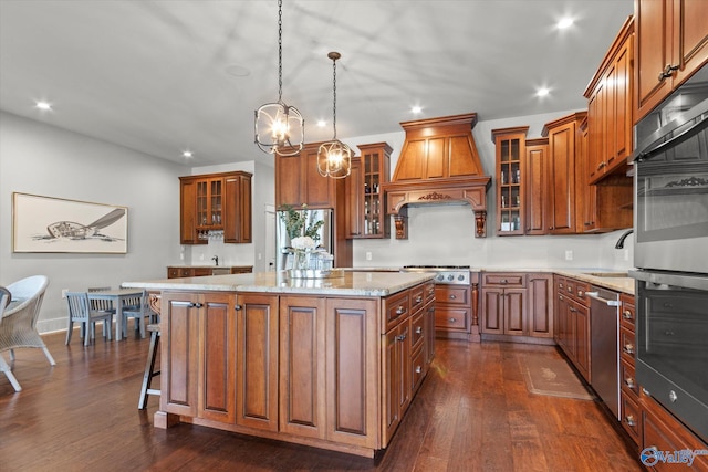 kitchen with premium range hood, decorative light fixtures, a center island, appliances with stainless steel finishes, and light stone countertops