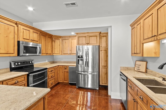 kitchen featuring appliances with stainless steel finishes, light stone countertops, sink, and dark tile patterned flooring