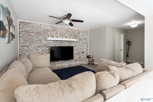 living room with ceiling fan, hardwood / wood-style floors, a textured ceiling, and a brick fireplace